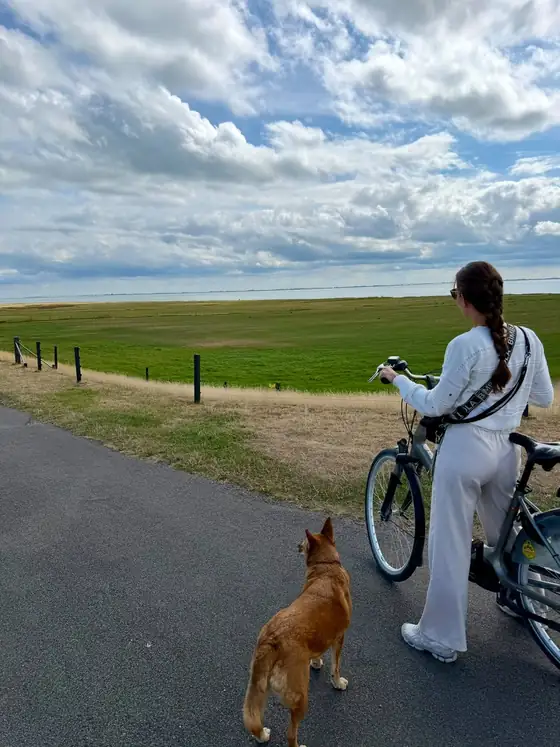 Romina mit Fahrrad und Hund an einem Weg entlang grüner Wiesen
